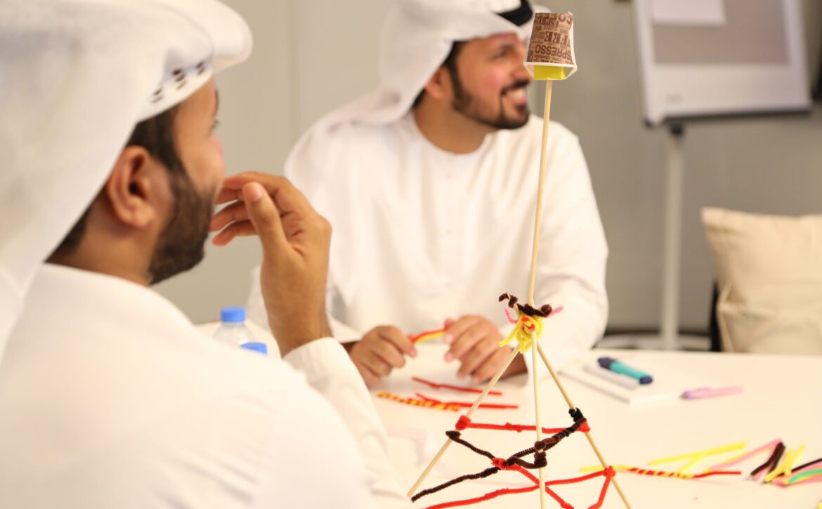 Two young men smiling as they build a tower out of various office supplies.